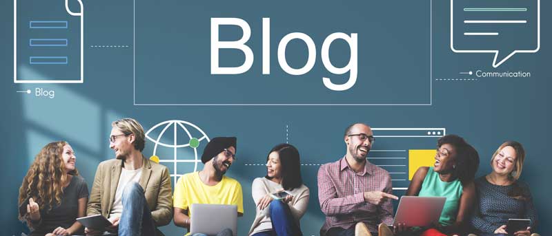 Groupe de personnes souriantes discutant autour d’ordinateurs portables devant un fond illustré avec le mot Blog